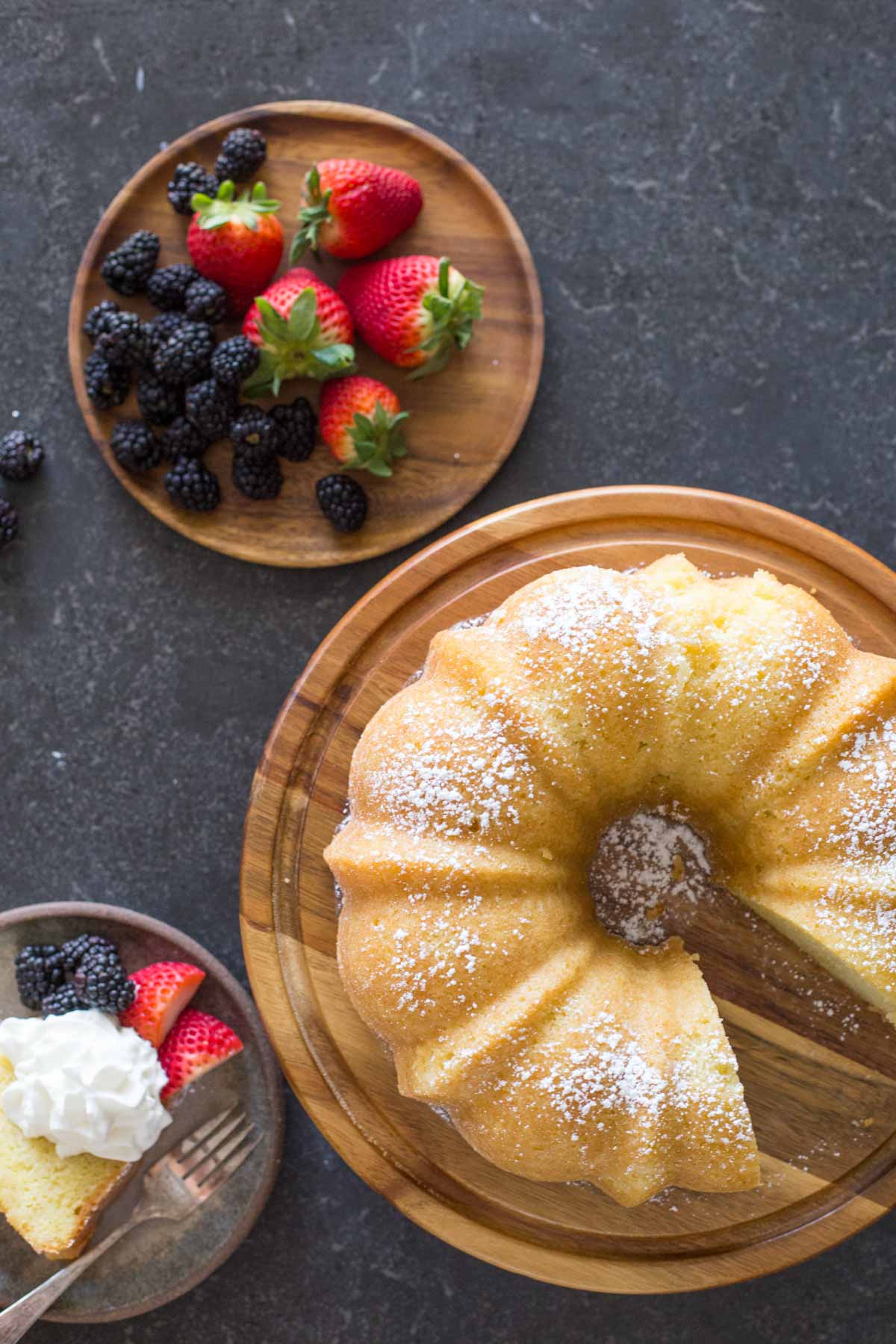 Kentucky Butter Cake on wooden cake stand with whipped cream and berries on a grey background.