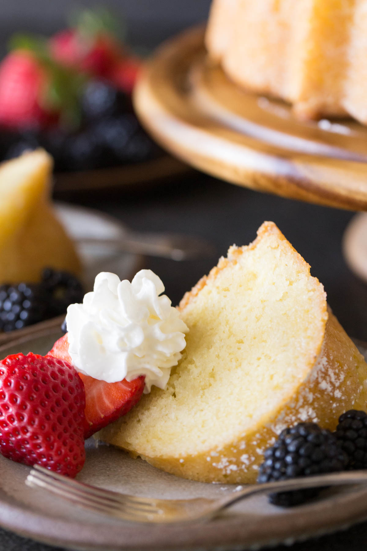 Kentucky Butter Cake on wooden cake stand with whipped cream and berries on a grey background.