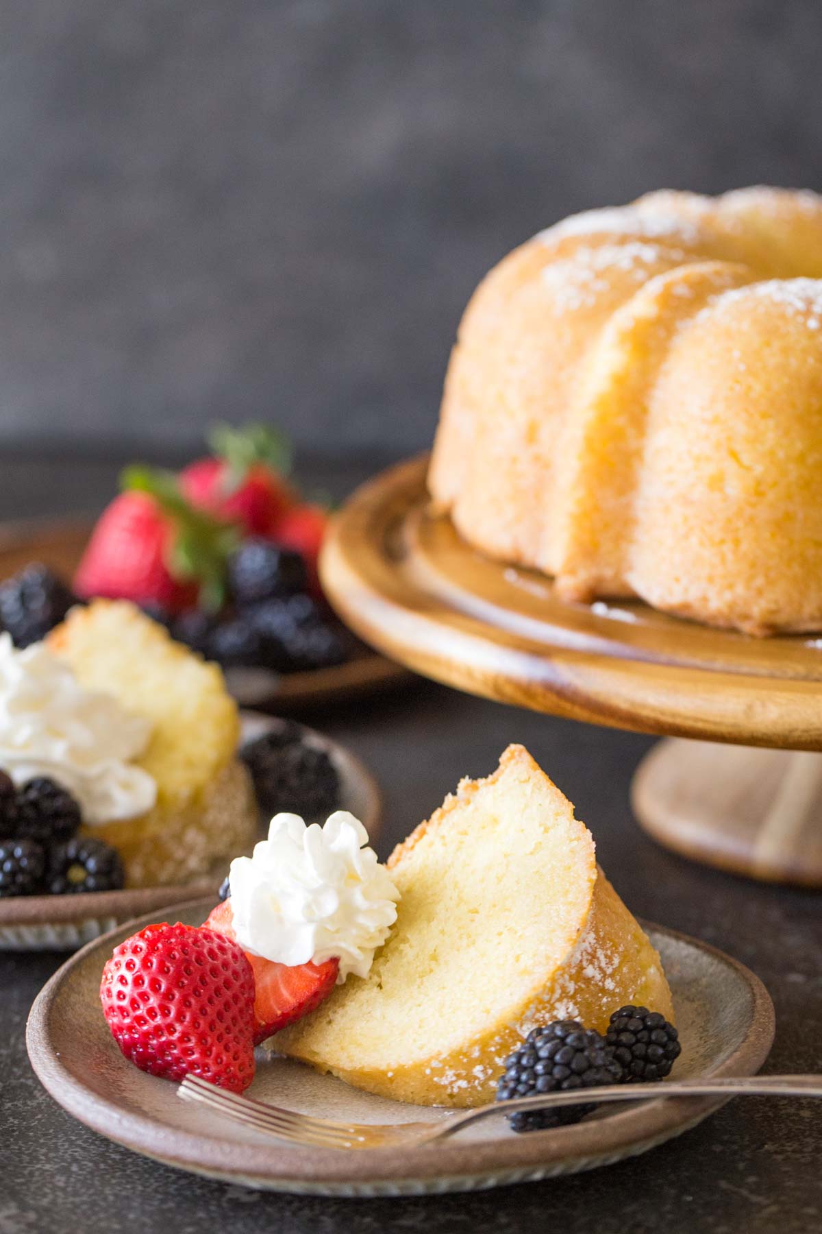 Kentucky Butter Cake on wooden cake stand with whipped cream and berries on a grey background.