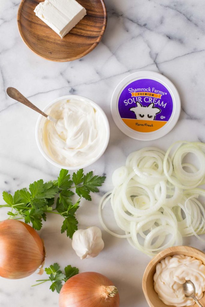 Prep ingredients for Bowl of Roasted Garlic and Caramelized Onion Dip on a white marble background.