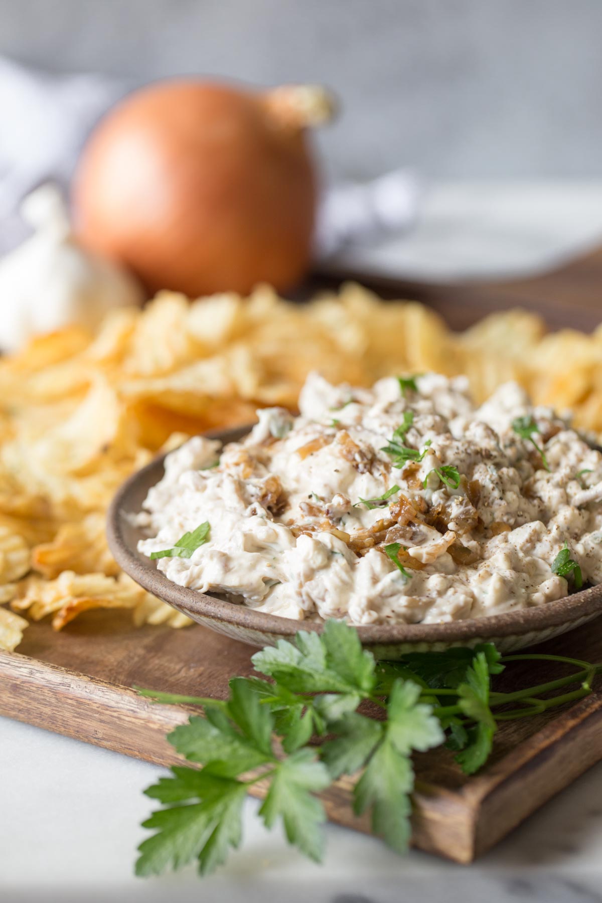 Bowl of Roasted Garlic and Caramelized Onion Dip on a platter with chips.