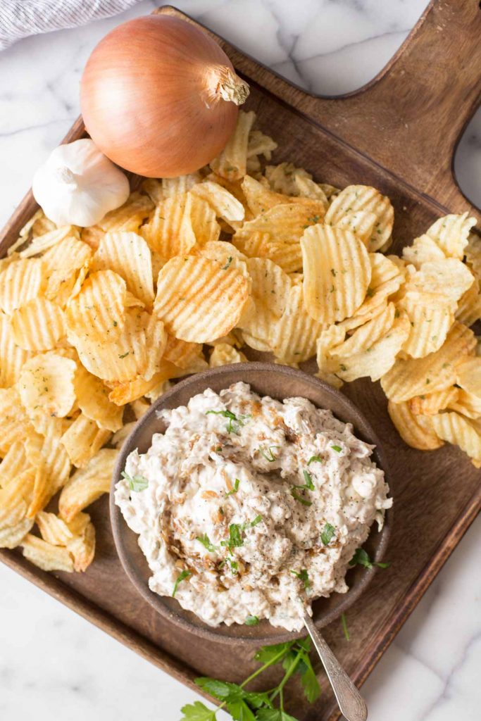 Overhead shot of Bowl of Roasted Garlic and Caramelized Onion Dip on a platter with chips.