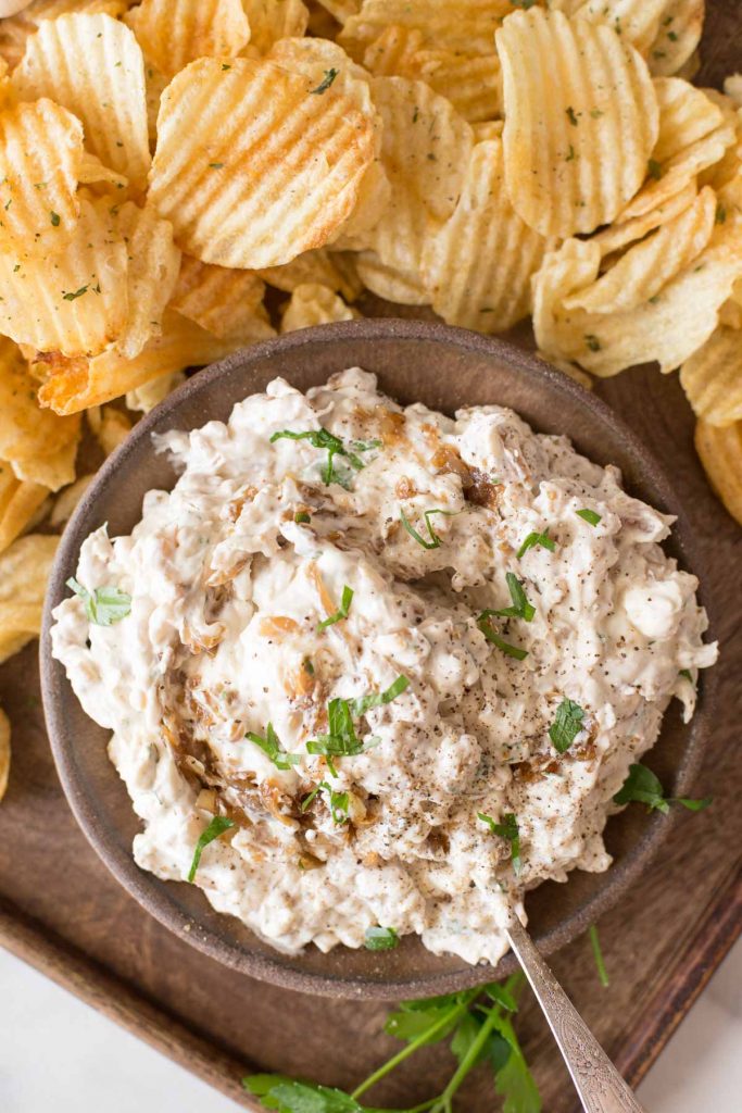 Bowl of Roasted Garlic and Caramelized Onion Dip on a platter with chips.