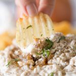 Chip dipping into bowl of Roasted Onion and Caramelized Onion Dip.