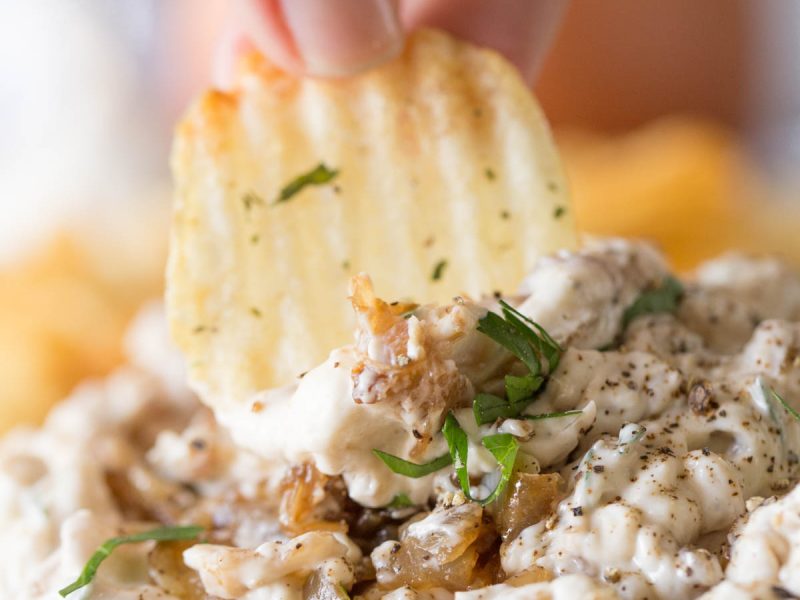 Chip dipping into bowl of Roasted Onion and Caramelized Onion Dip.