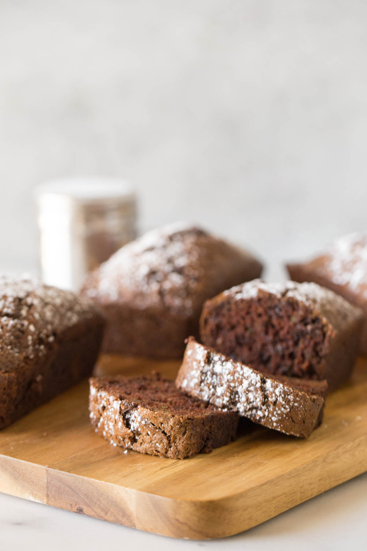 Loaves of Chocolate Zucchini Bread arranged on a wooden cutting board with a white background.