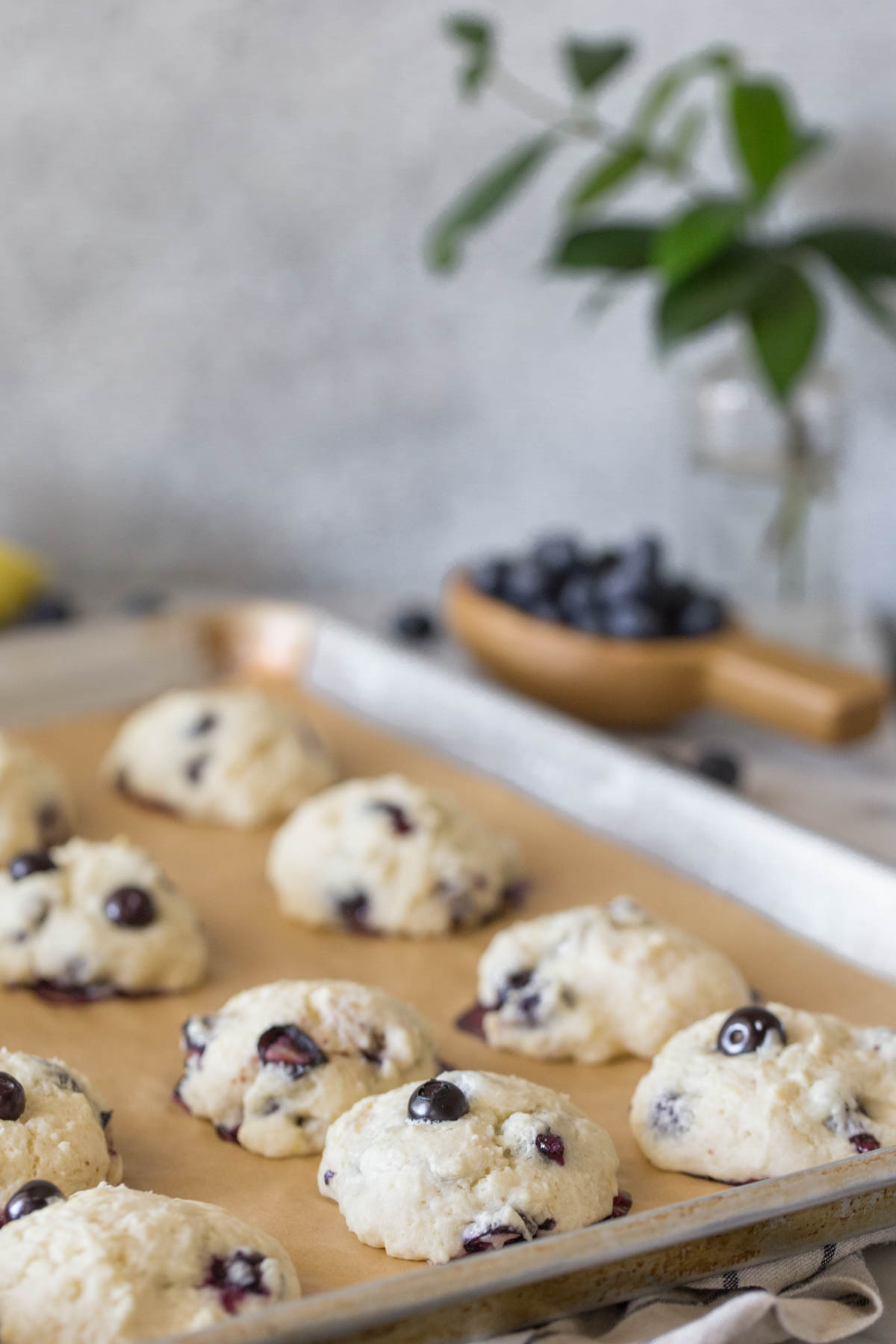 Glazed Lemon Blueberry Muffin Tops on a baking sheet with a grey background.