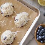Glazed Lemon Blueberry Muffin Tops on a baking sheet with a grey background.