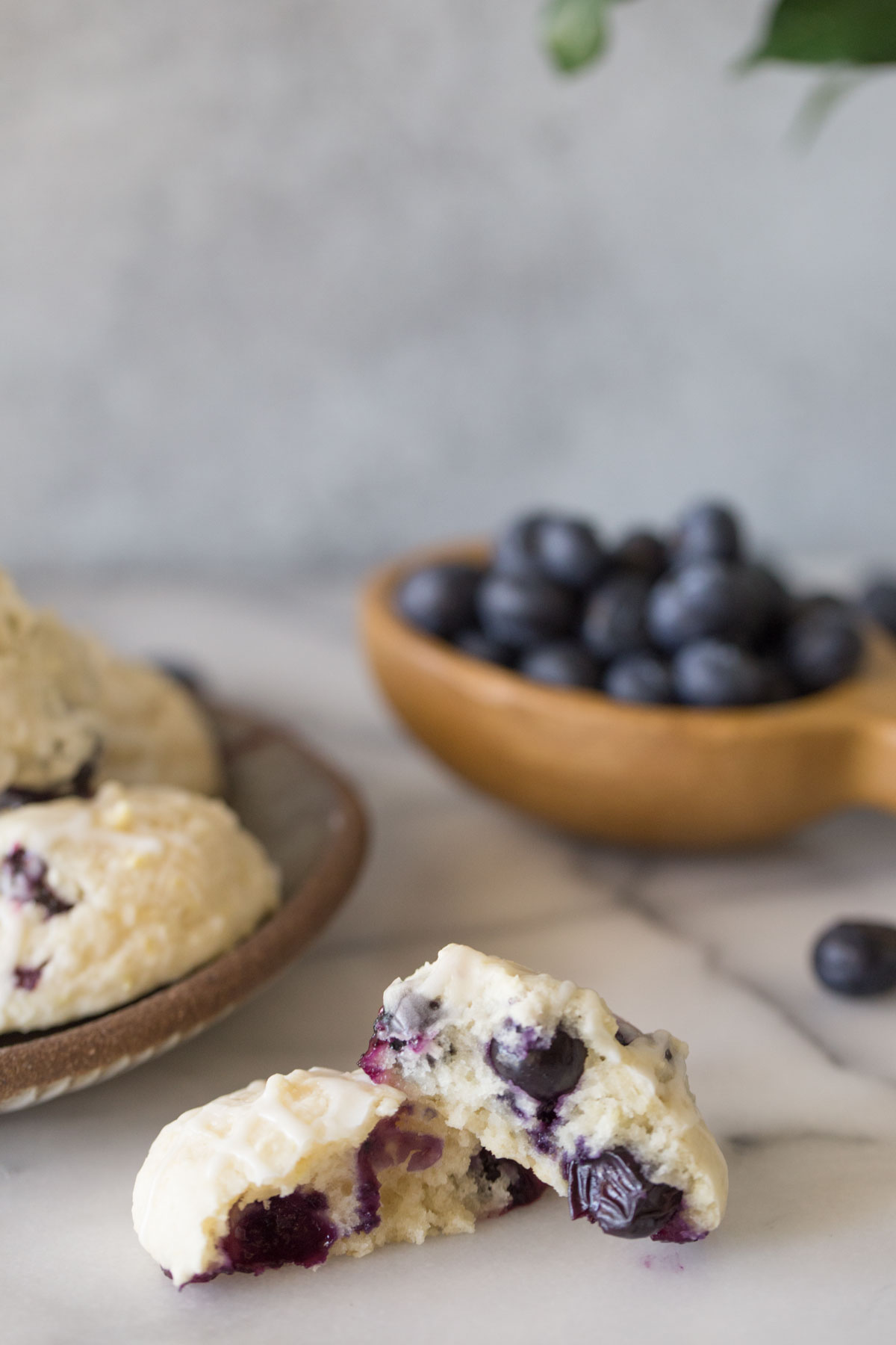 Close up shot of the inside of a halved Glazed Lemon Blueberry Muffin Top with fresh blueberries in the background.