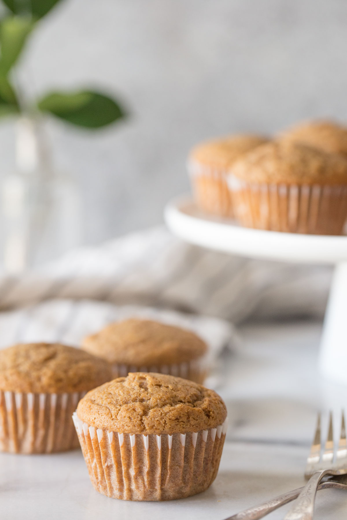 Cinnamon Applesauce Muffins on a white marble board with a cake stand in the background.