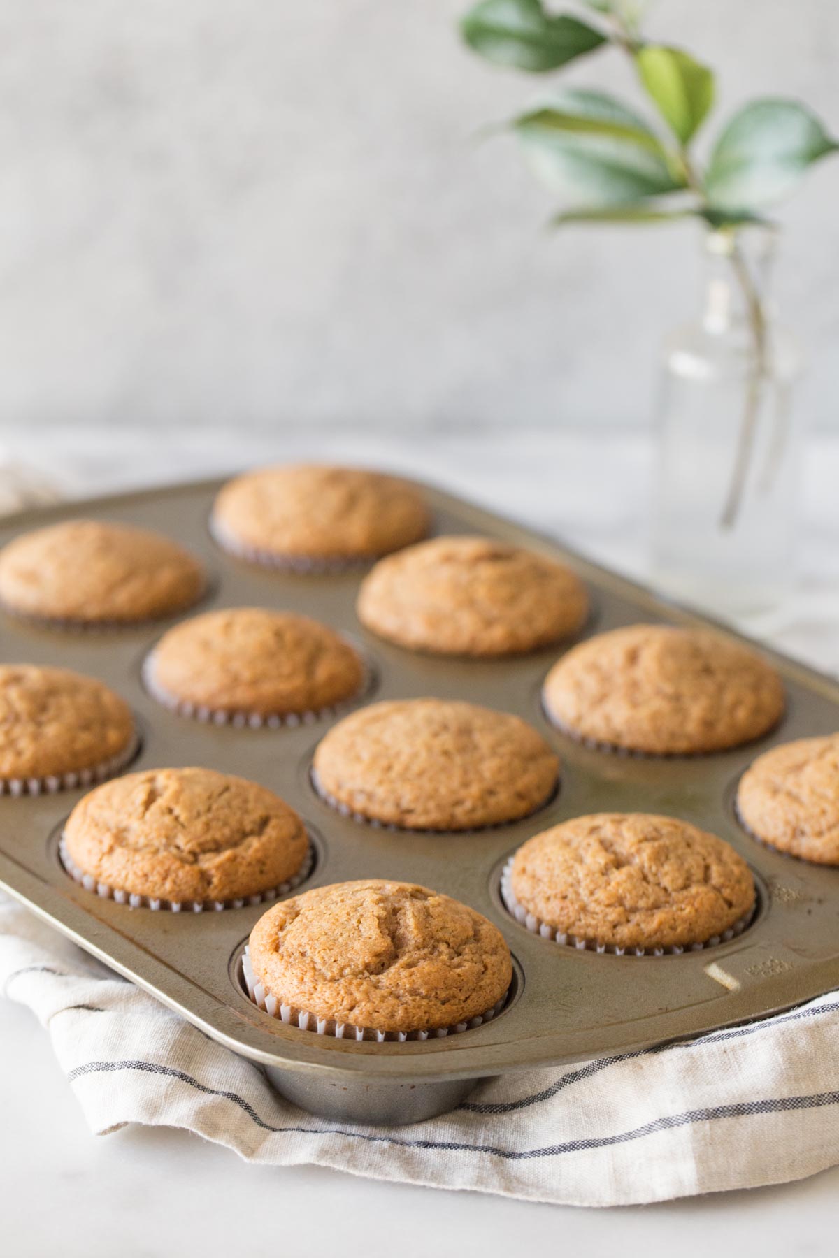 A muffin tin full of Cinnamon Applesauce Muffins with a white marble background.