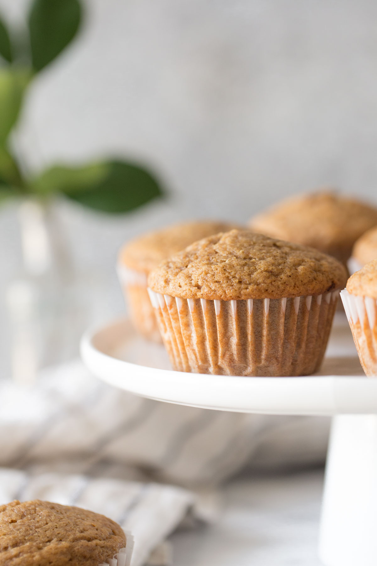 Cinnamon Applesauce Muffins on a white cake stand with a white background.