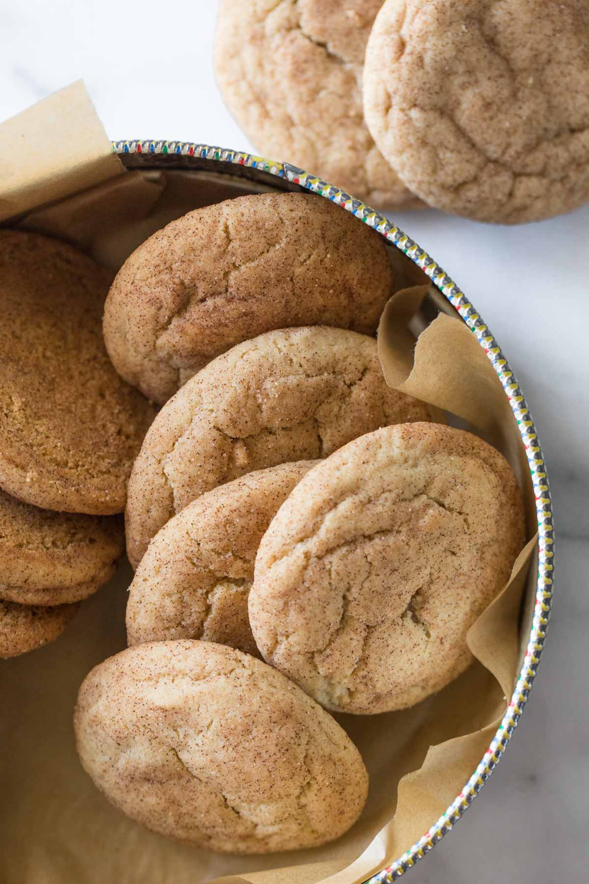 Overhead view of Super Soft Snickerdoodles in a cookie tin on a white marble background.