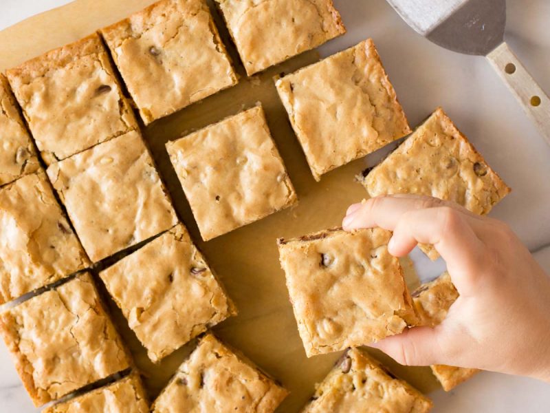 Overhead view of blondies with a child's hand taking one.