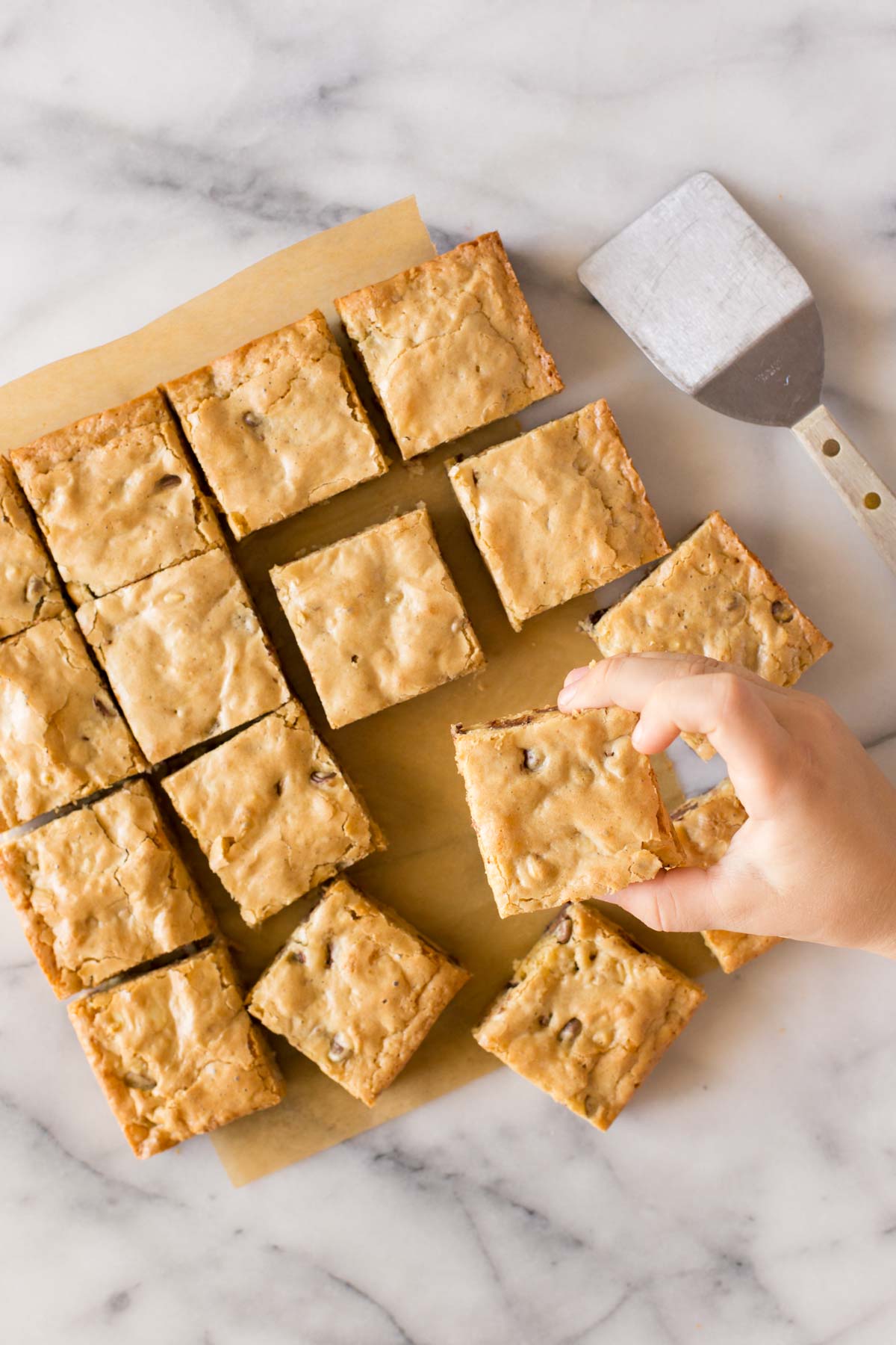 Overhead view of blondies with a child's hand taking one.