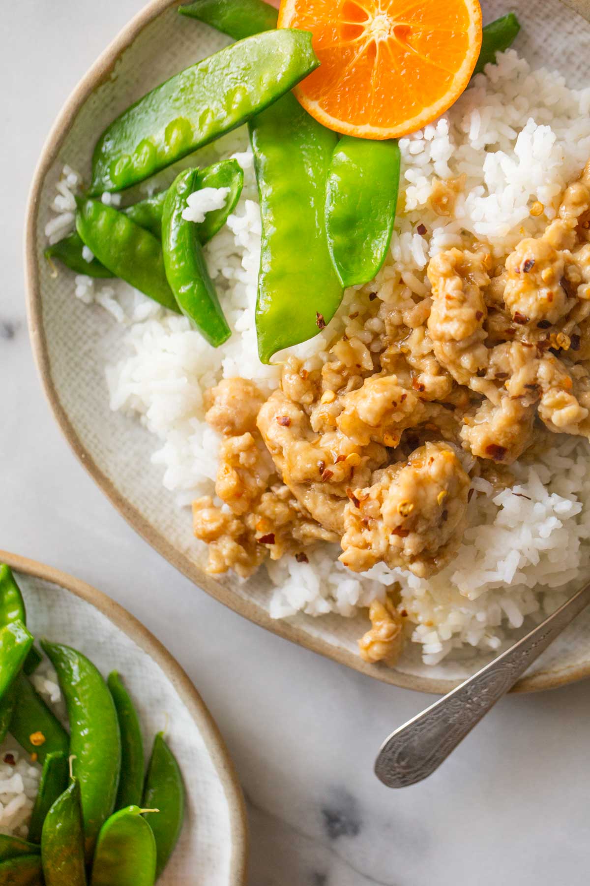 A close up overhead shot of Easy Orange Chicken over rice with snow peas. 