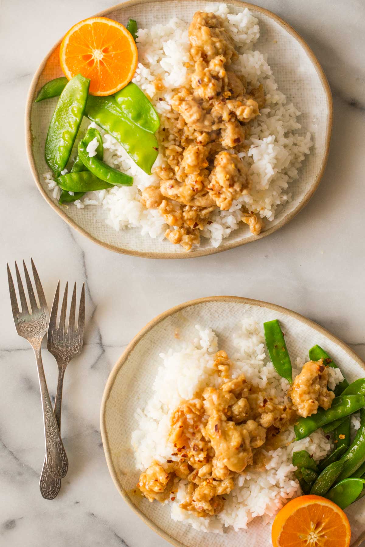 Overhead shot of two plates of Easy Orange Chicken on a white marble background. 