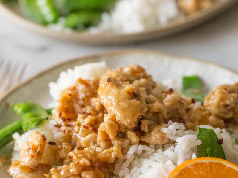 Two plates of Easy Orange Chicken with white rice and snow peas.