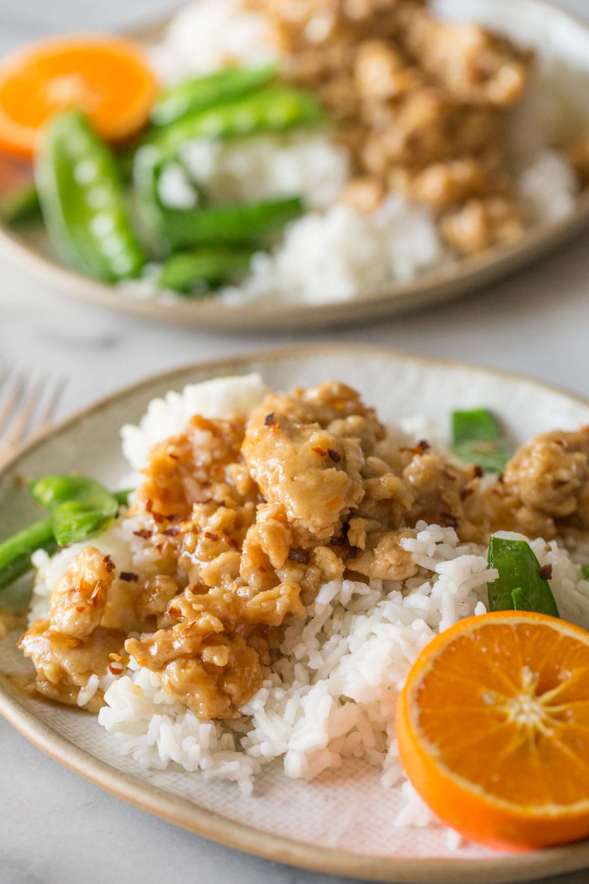 Two plates of Easy Orange Chicken with white rice and snow peas.