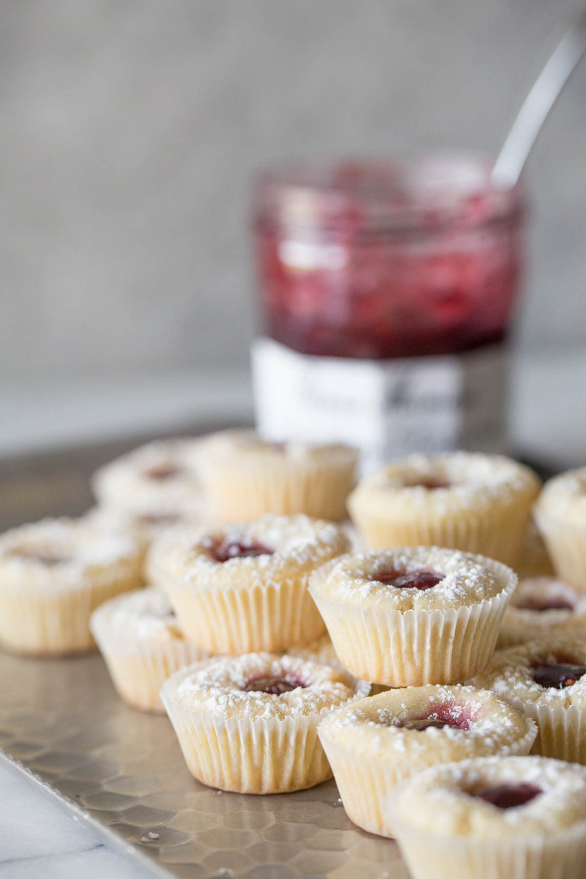 Stacked Mini Raspberry Almond Tarts on a sliver tray with a jelly jar in the background.