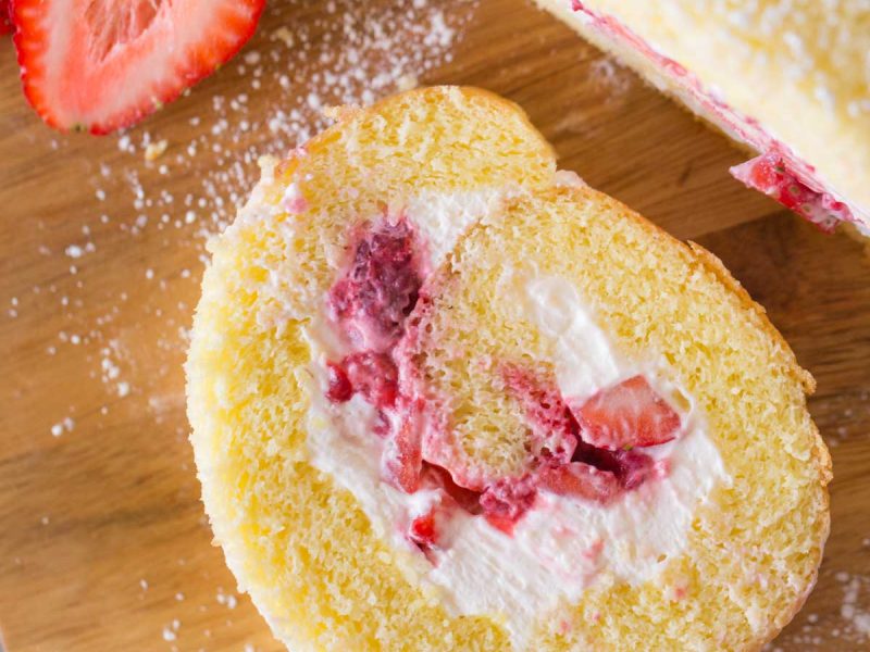 Close up overhead view of sliced Vanilla Roll Cake on a wooden cutting board.