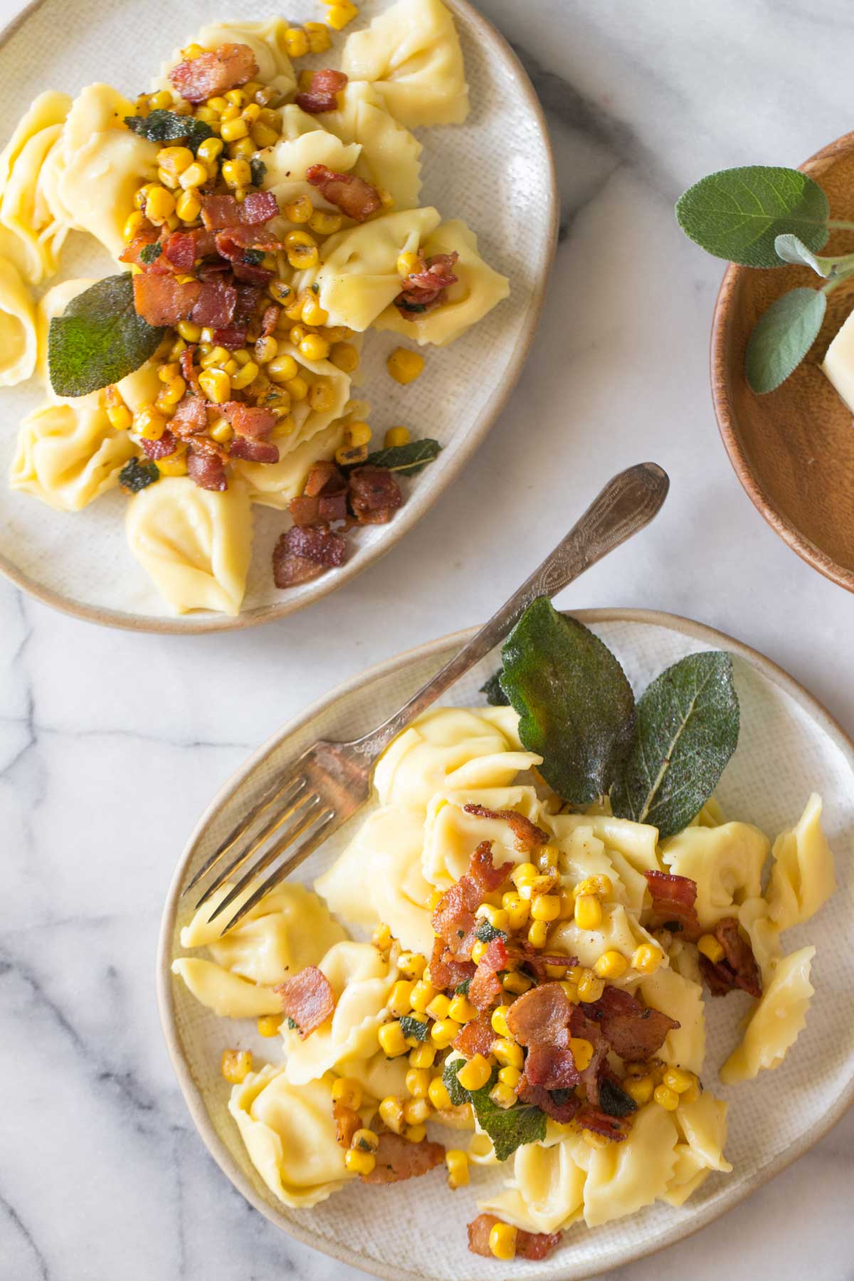 Overhead view of two plates of Creamy Tortellini With Bacon and Corn on a marble background.