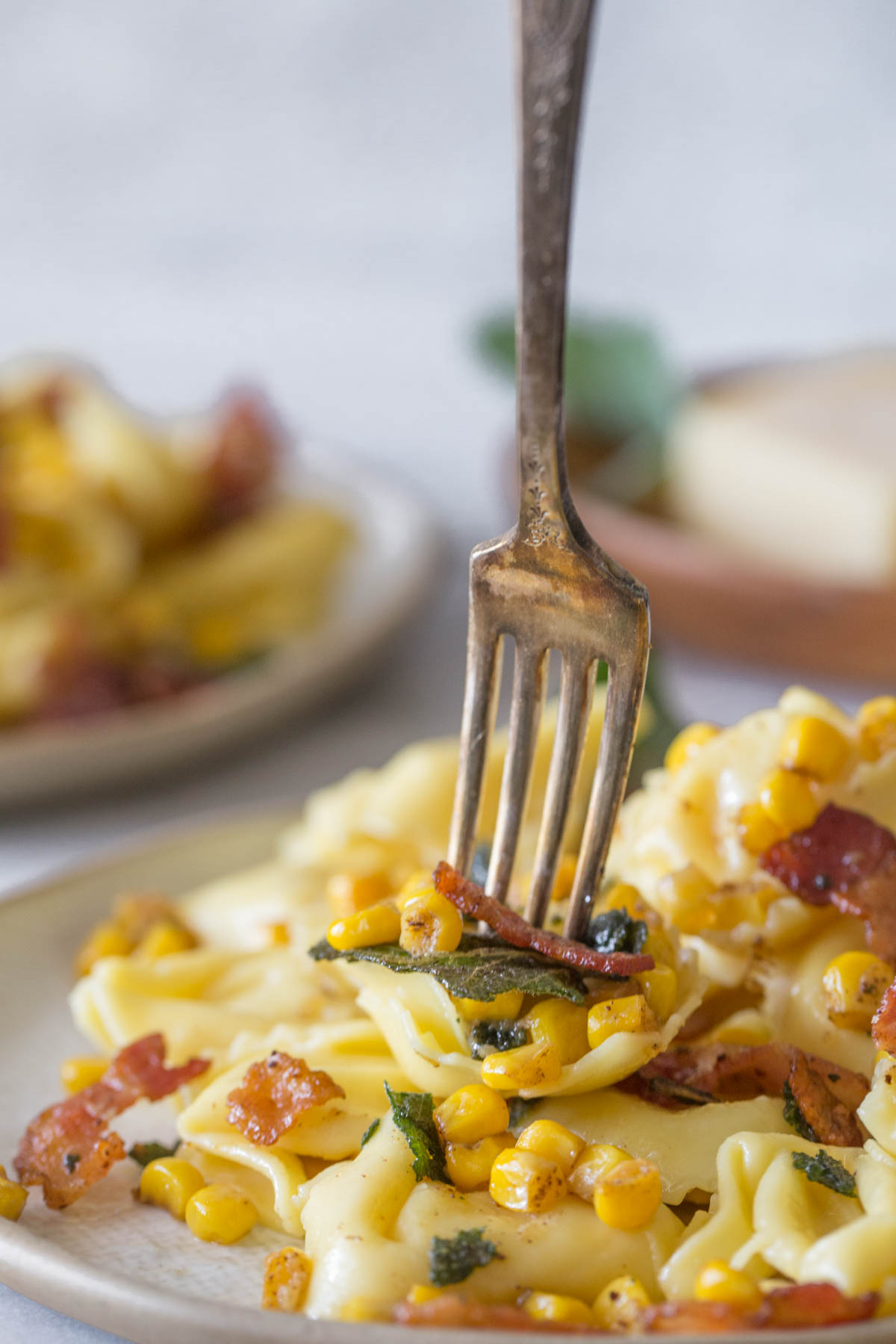 Close up shot of a fork in a plate of Creamy Tortellini With Bacon and Corn.