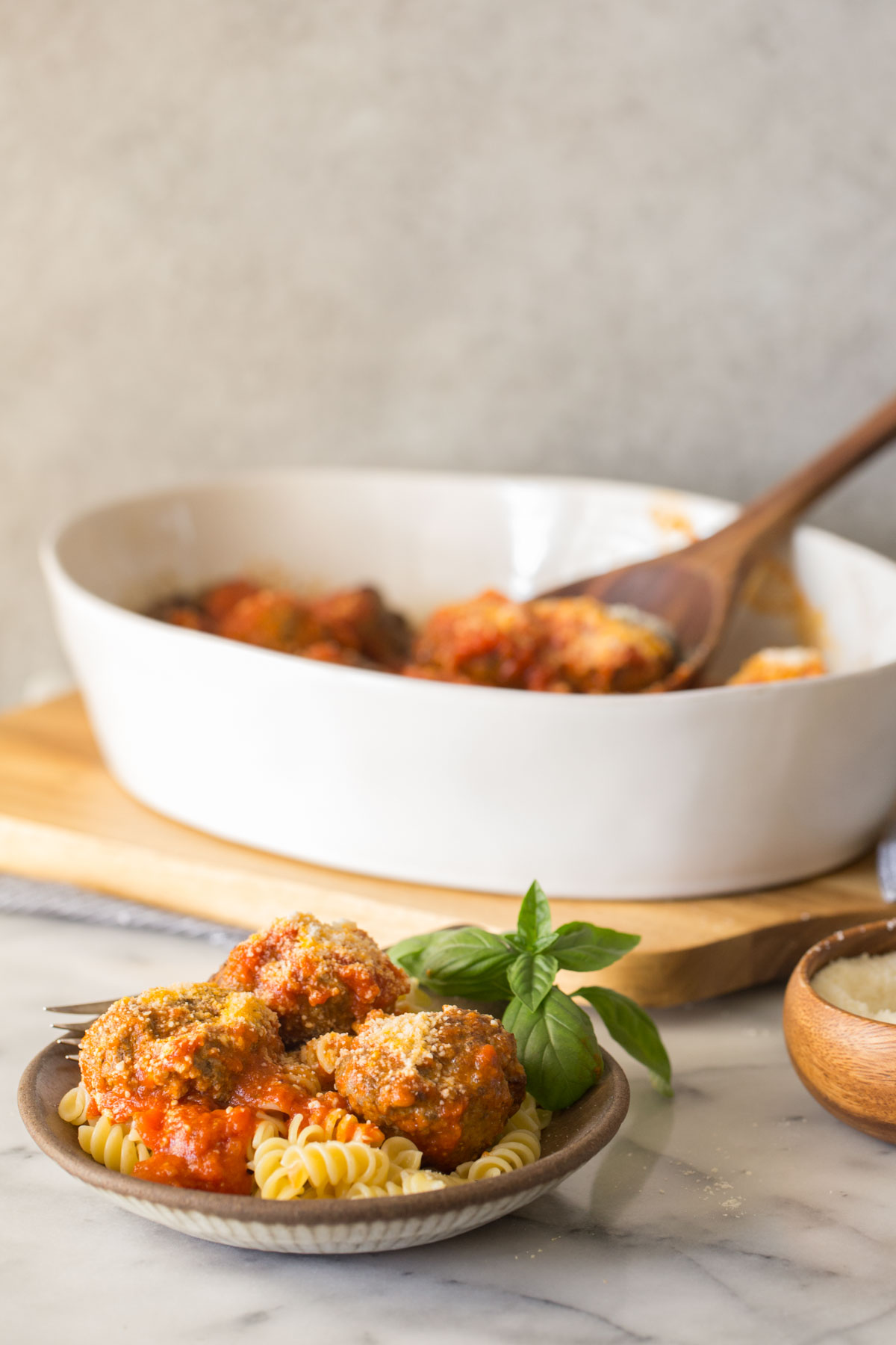 Easy Broiled Italian Meatballs served over rotini pasta in a bowl, with a baking dish of more meatballs in the background.