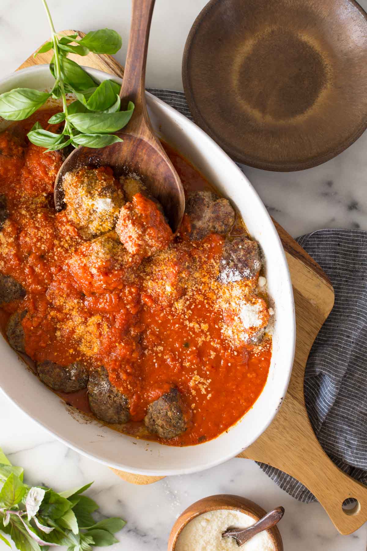 Overhead shot of Easy Broiled Italian Meatballs in a baking dish sitting on a wooden cutting board, with a wood serving spoon in the meatballs.
