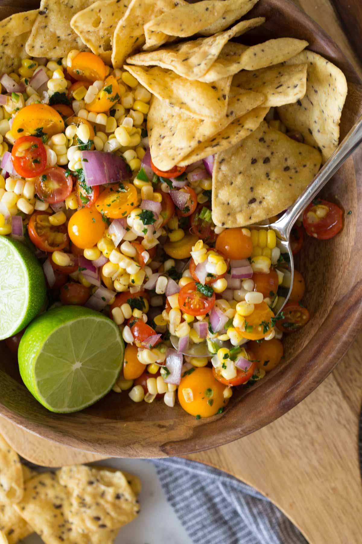 Overhead shot of Honey Lime Corn Salsa in a wood serving bowl with a sliced lime and tortilla chips.