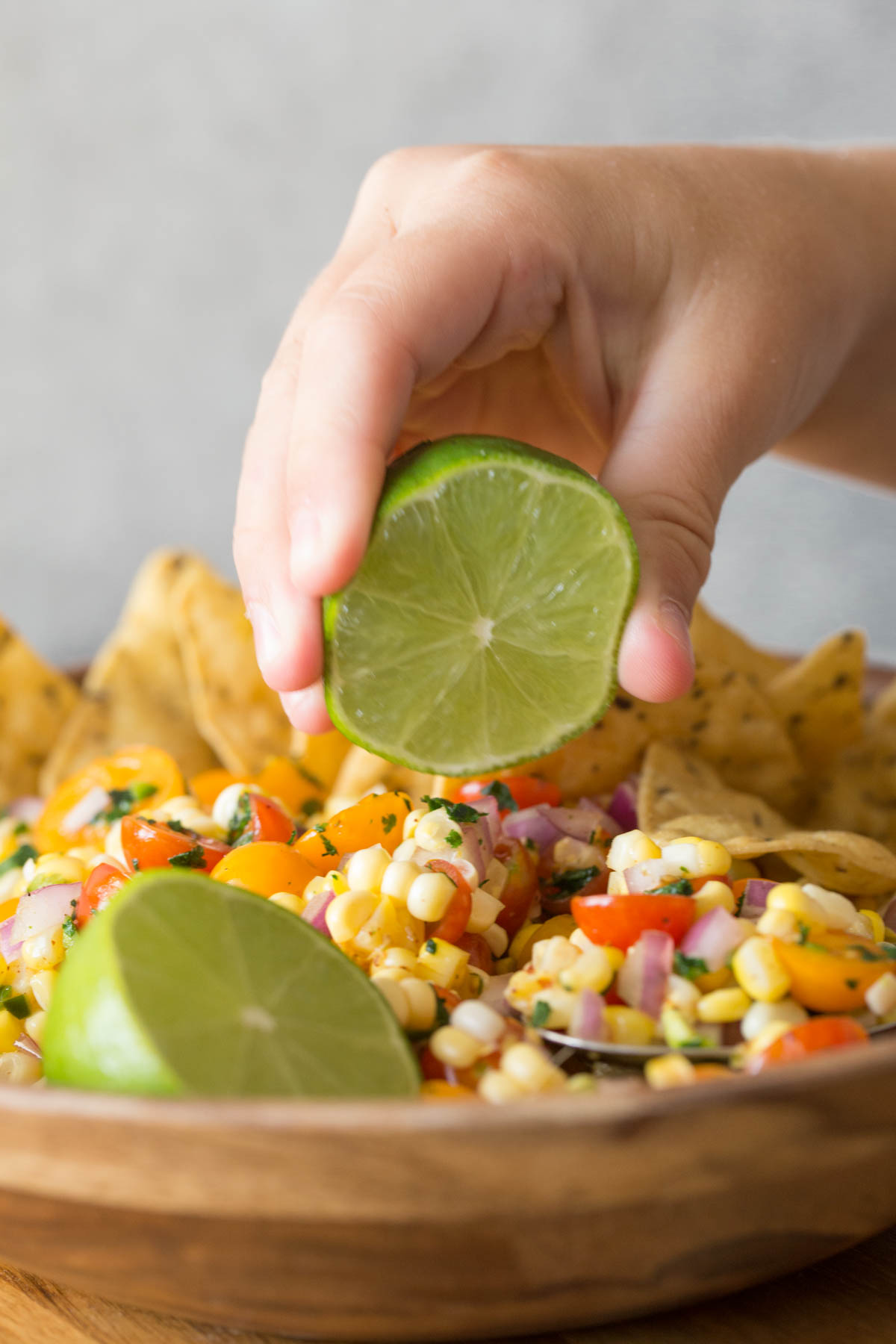 Close up shot of a hand squeezing a lime over a wooden bowl of Honey Lime Corn Salsa.