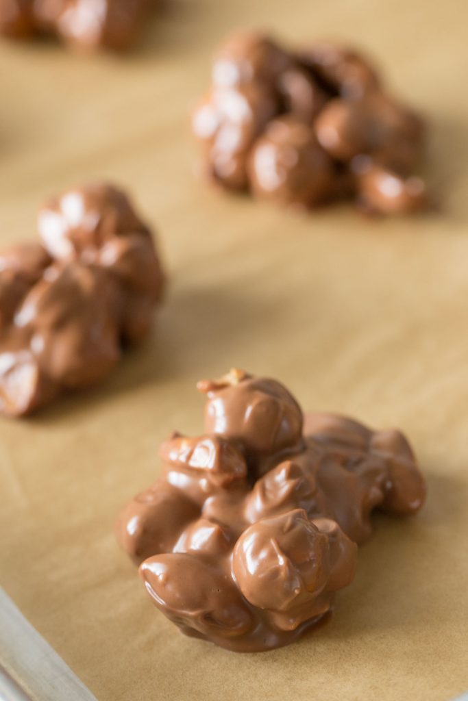 Close up shot of Chocolate Peanut Clusters on a parchment lined baking sheet.
