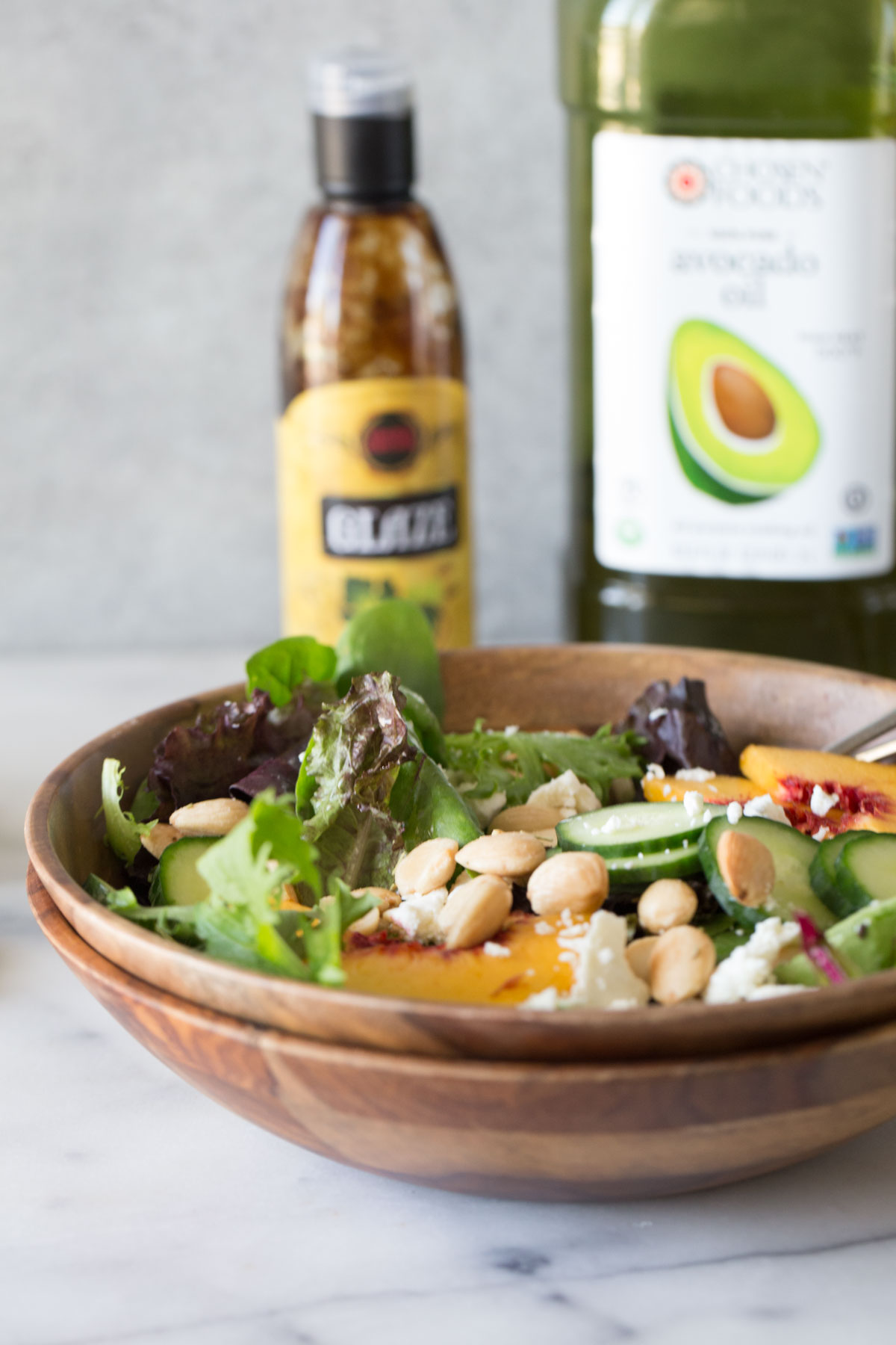 Summer Peach Salad in a wood bowl with a bottle of balsamic glaze and avocado oil in the background.