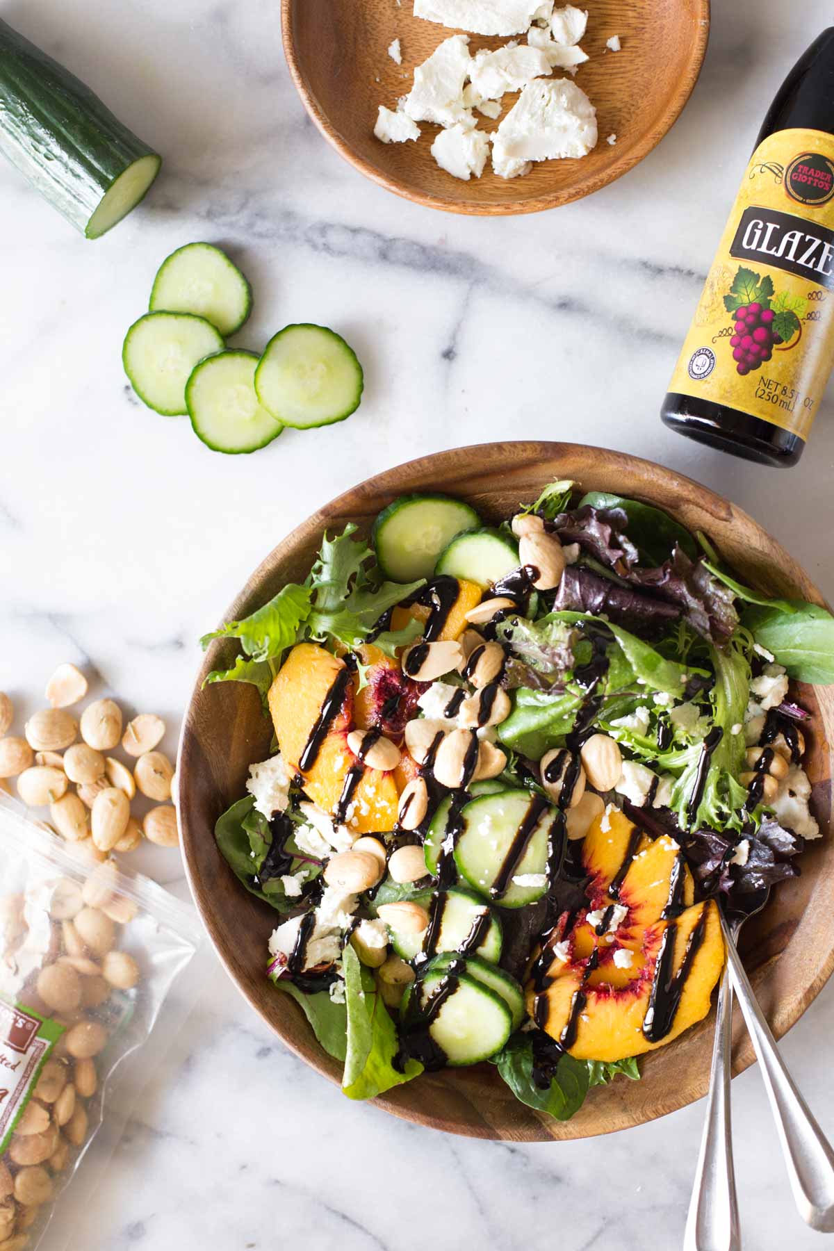 Overhead shot of Summer Peach Salad in a wood bowl on a marble background with ingredients of the salad around the bowl.