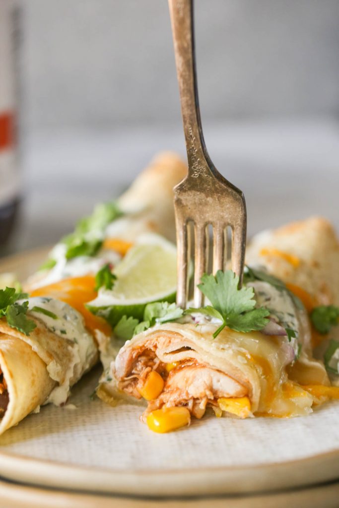 A fork stuck in a BBQ Chicken Taquito on a plate with another BBQ Chicken Taquito.