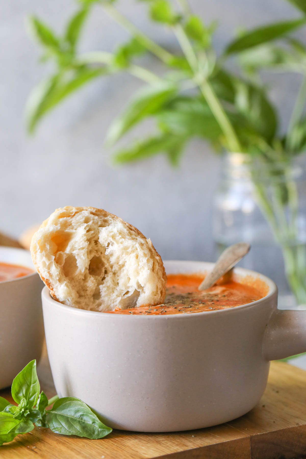 Close up shot of a bowl of Creamy Balsamic Tomato Soup with a torn piece of crusty bread dipped into it.
