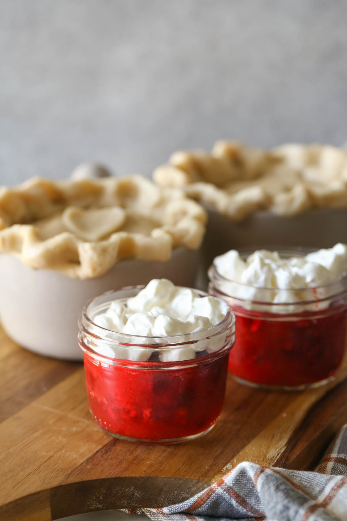 Two mini mason jars of Raspberry Jello Salad sitting on a cutting board with two mini chicken pot pies in the background.