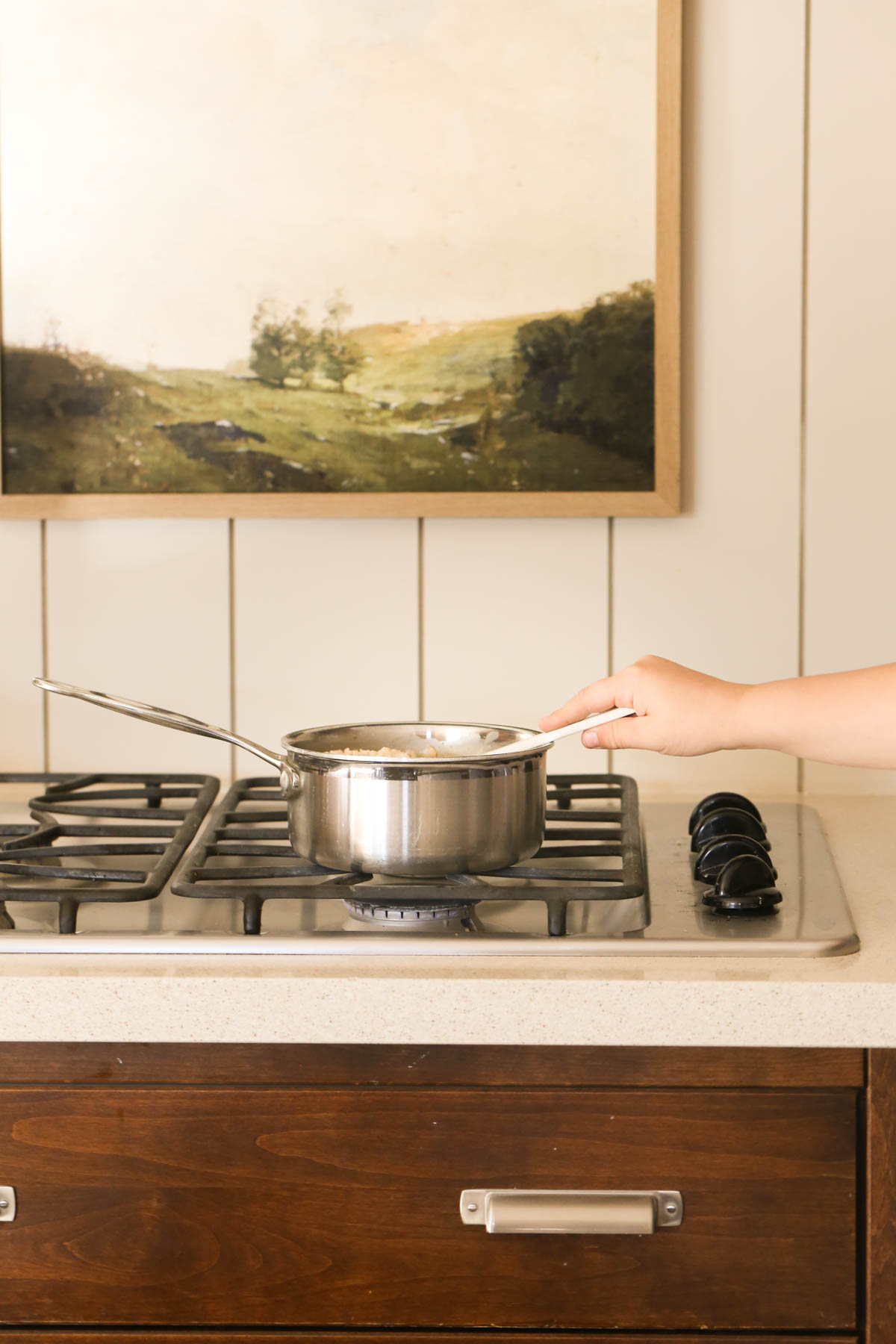 A pot of oatmeal on a gas stove top with a hand on the stirring utensil. 