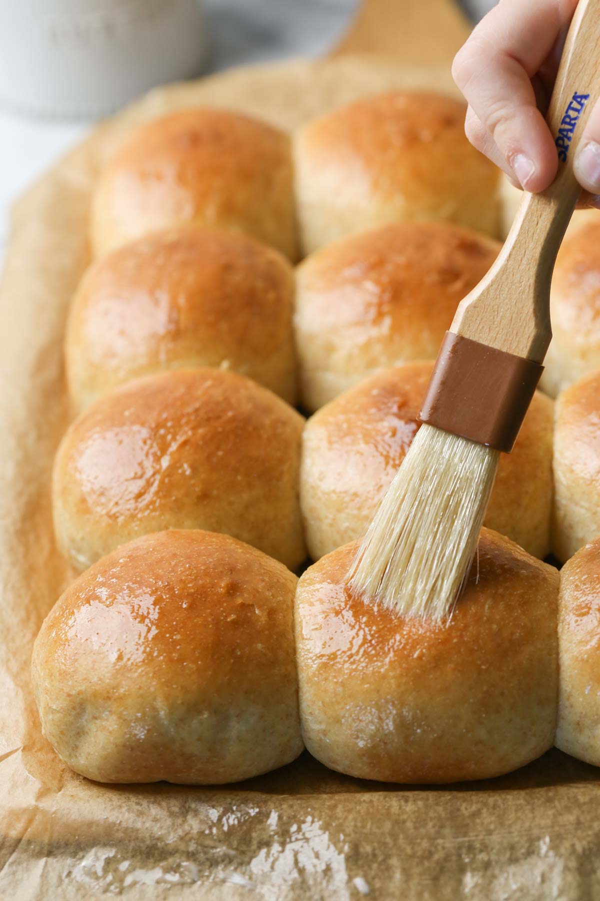 Close up shot of Overnight Honey Wheat Rolls being brushed with melted butter.  