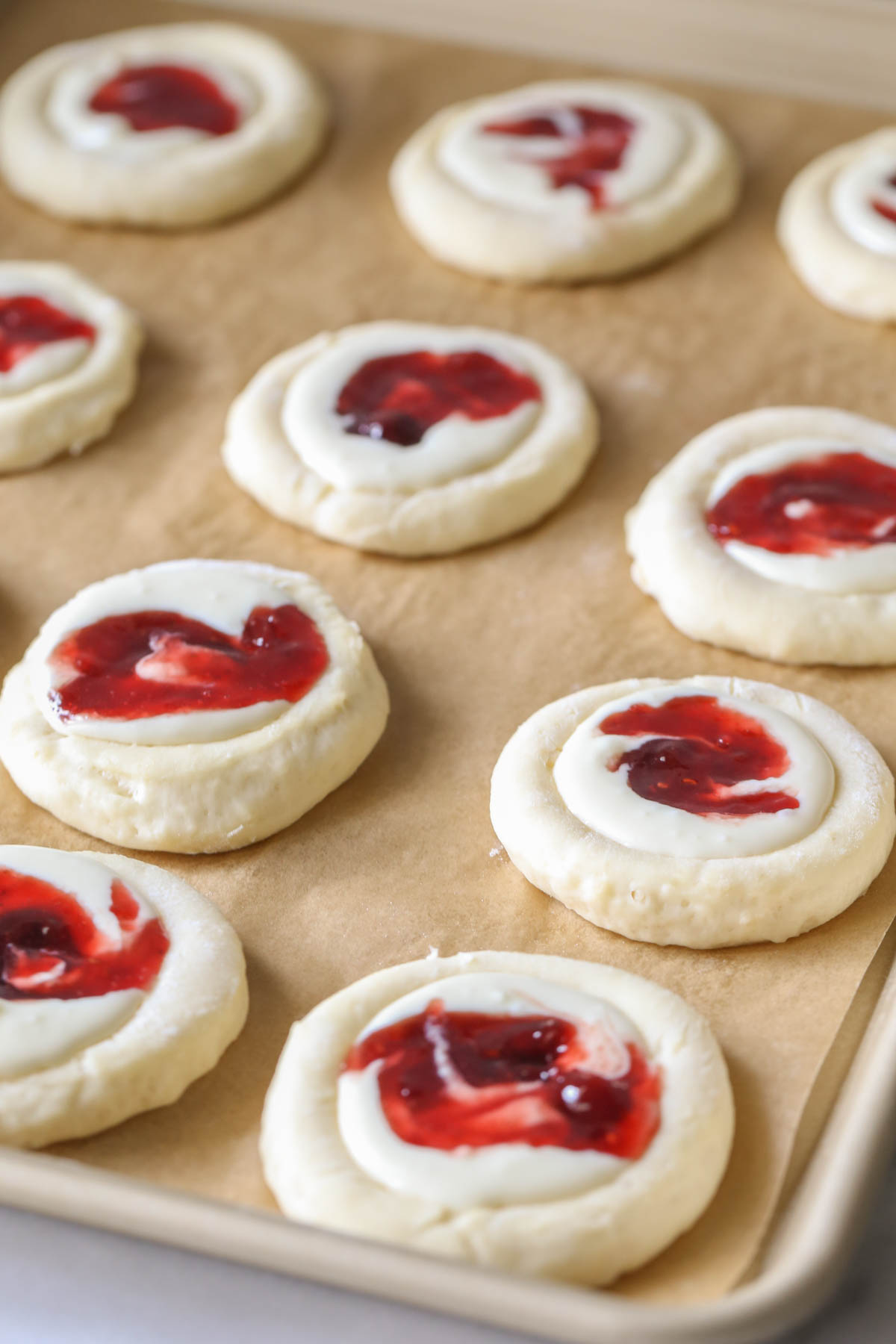 Raspberry Cream Cheese Kolaches arranged on a parchment lined baking sheet before being baked.  