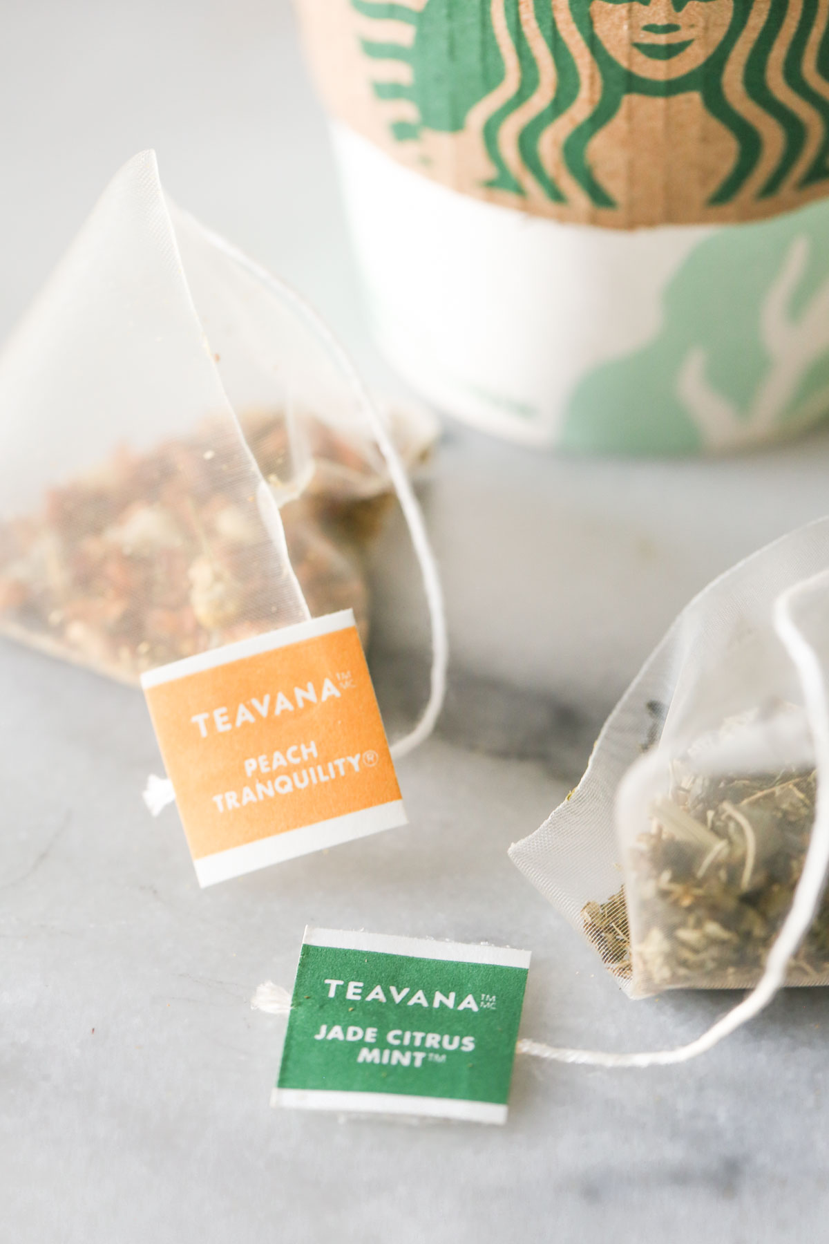Close up shot of a Teavana Peach Tranquility tea sachet next to a Teavana Jade Citrus Mint tea sachet, with a Starbucks cup in the background.