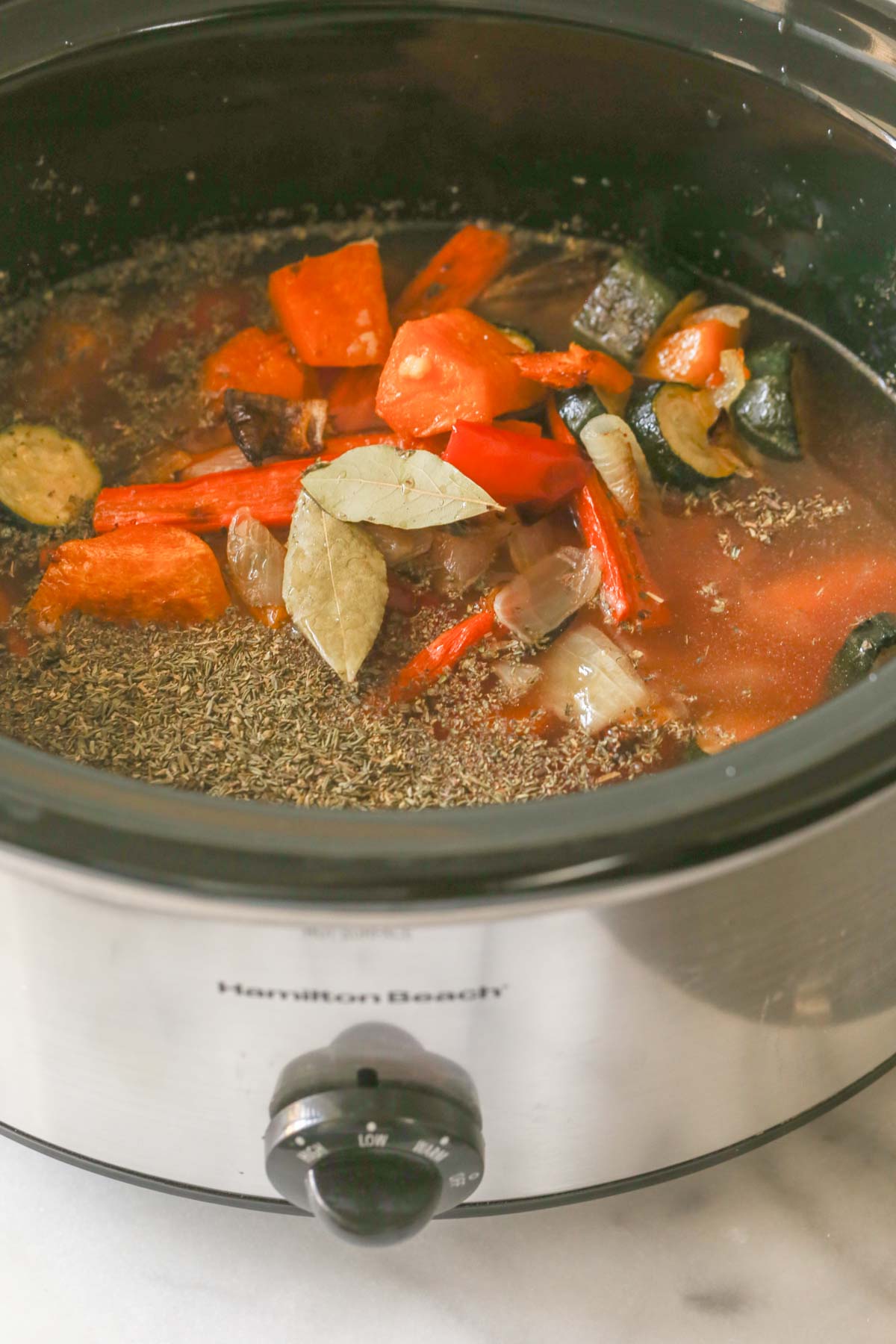 A crockpot with all the ingredients for the Roasted Vegetable Soup in it.