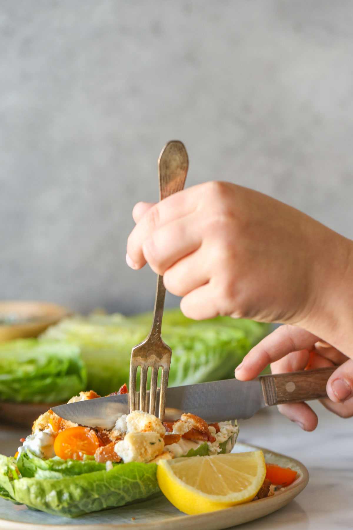 Two hands with a fork and a knife cutting into a Wedge Style BLT Salad on a plate.  