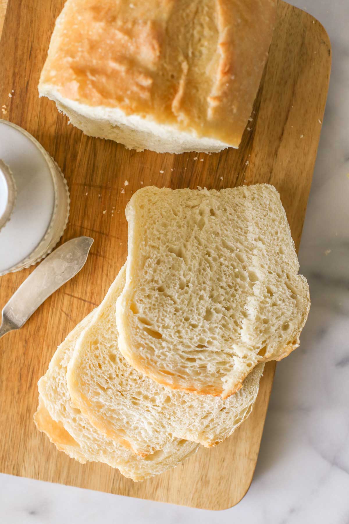 Overhead shot of a Sourdough Sandwich Loaf sliced on a cutting board with a butter keeper and butter knife next to the bread.