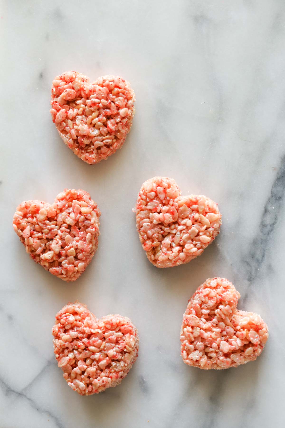 Overhead shot of five heart shaped Strawberry Rice Krispie Treats on a marble background.