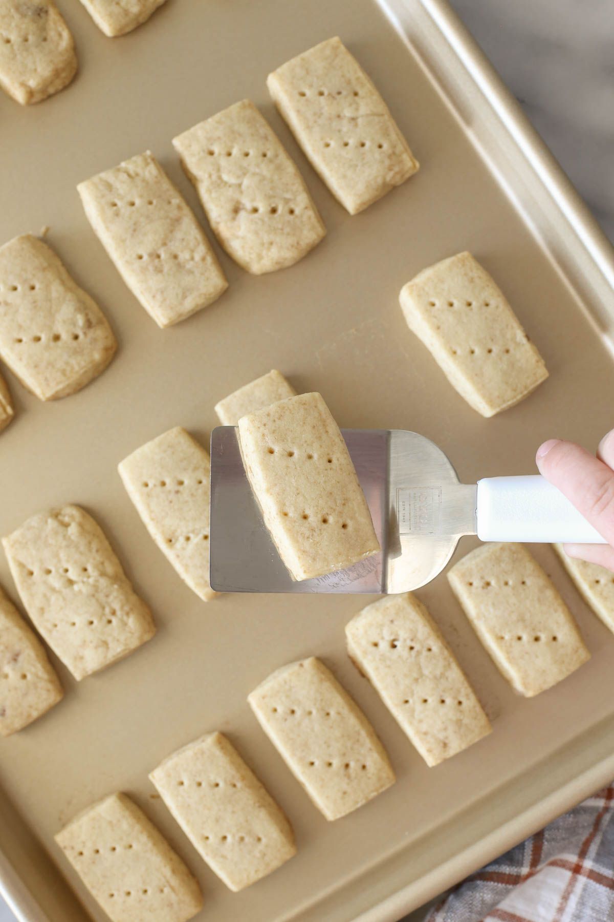 Overhead shot of a spatula with a Buttery Shortbread Cookie held over the baking sheet with more Buttery Shortbread Cookies.