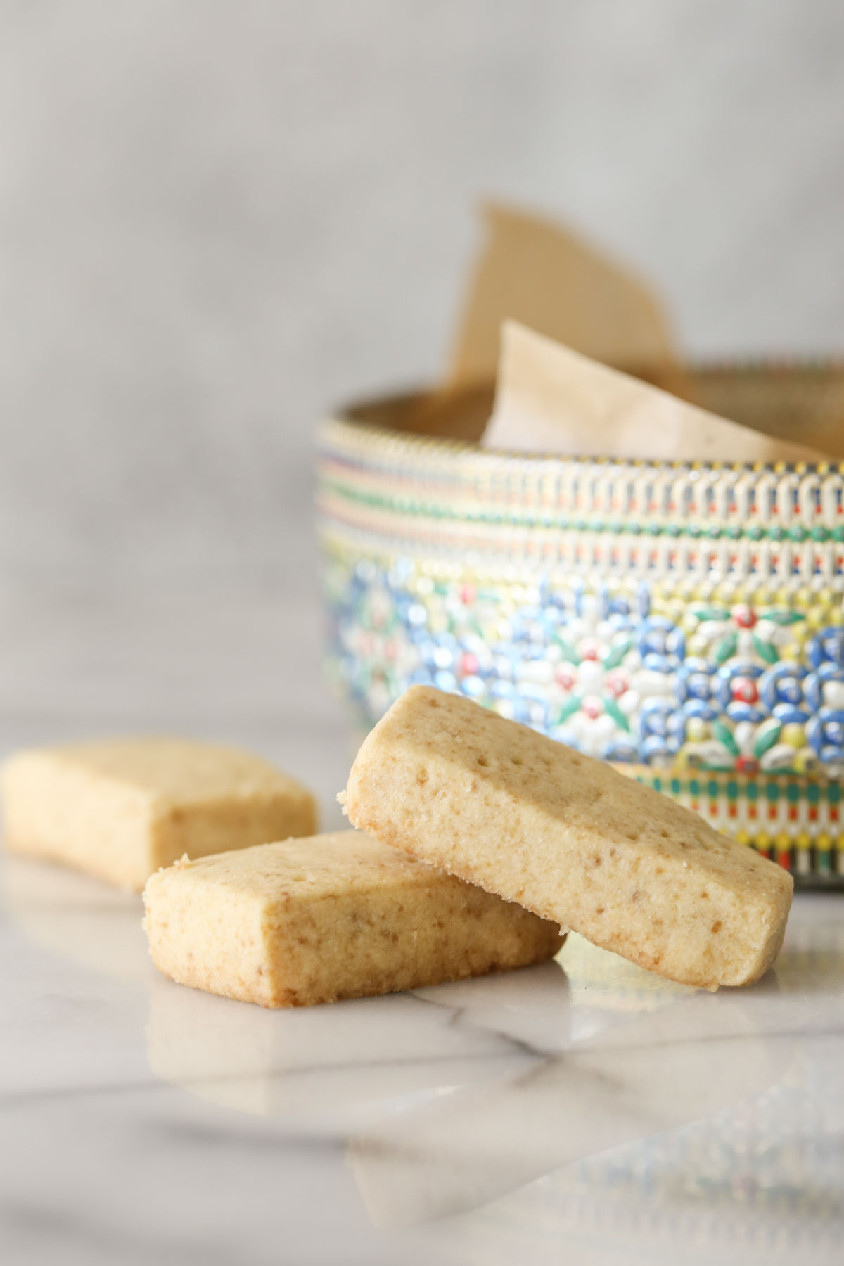 Close up shot of two Buttery Shortbread Cookies stacked, with another cookie in the background next to a colorful round cookie tin.