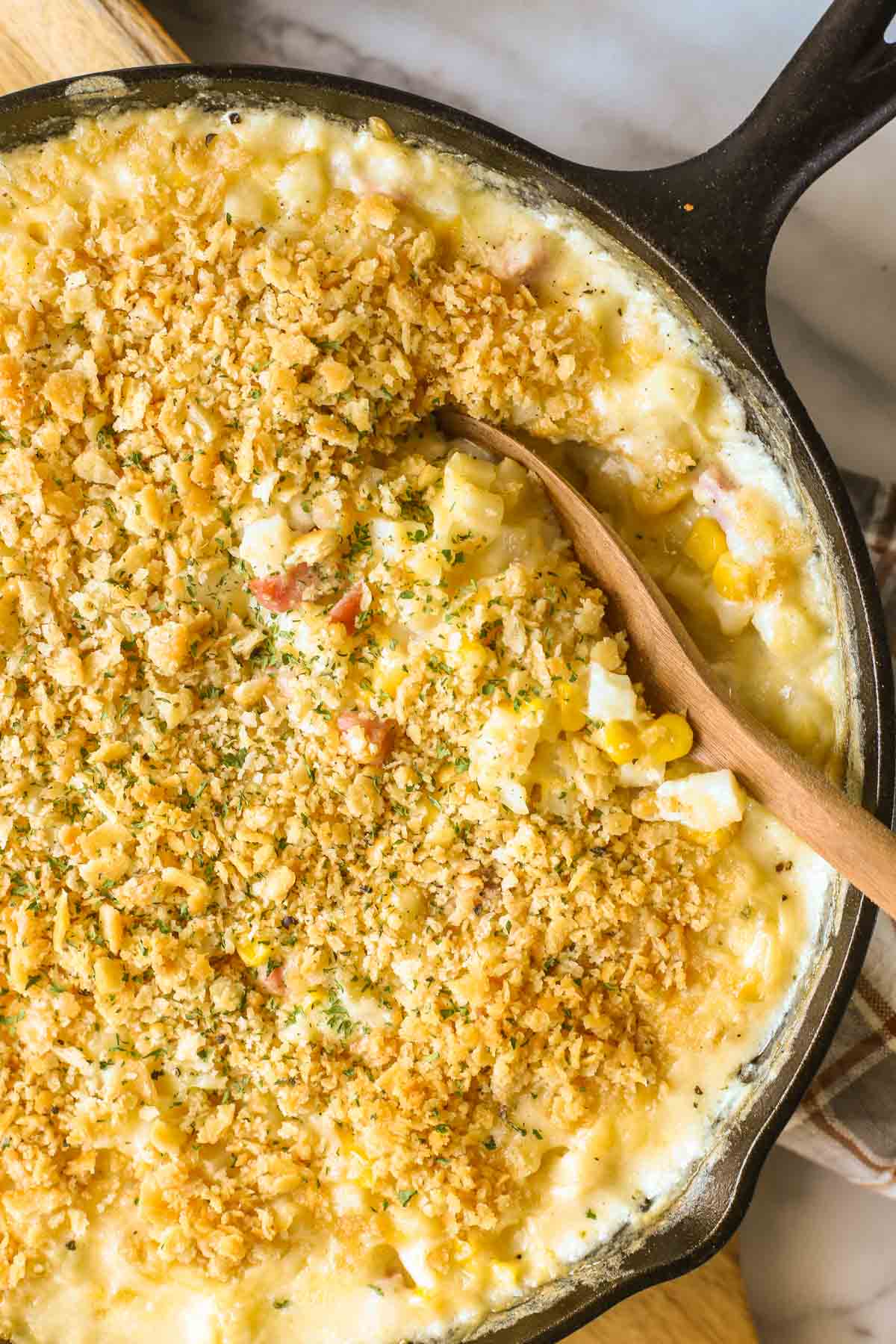 Close up overhead shot of Cheesy Ham and Potato Skillet in a cast iron skillet with a wooden serving spoon in it.  