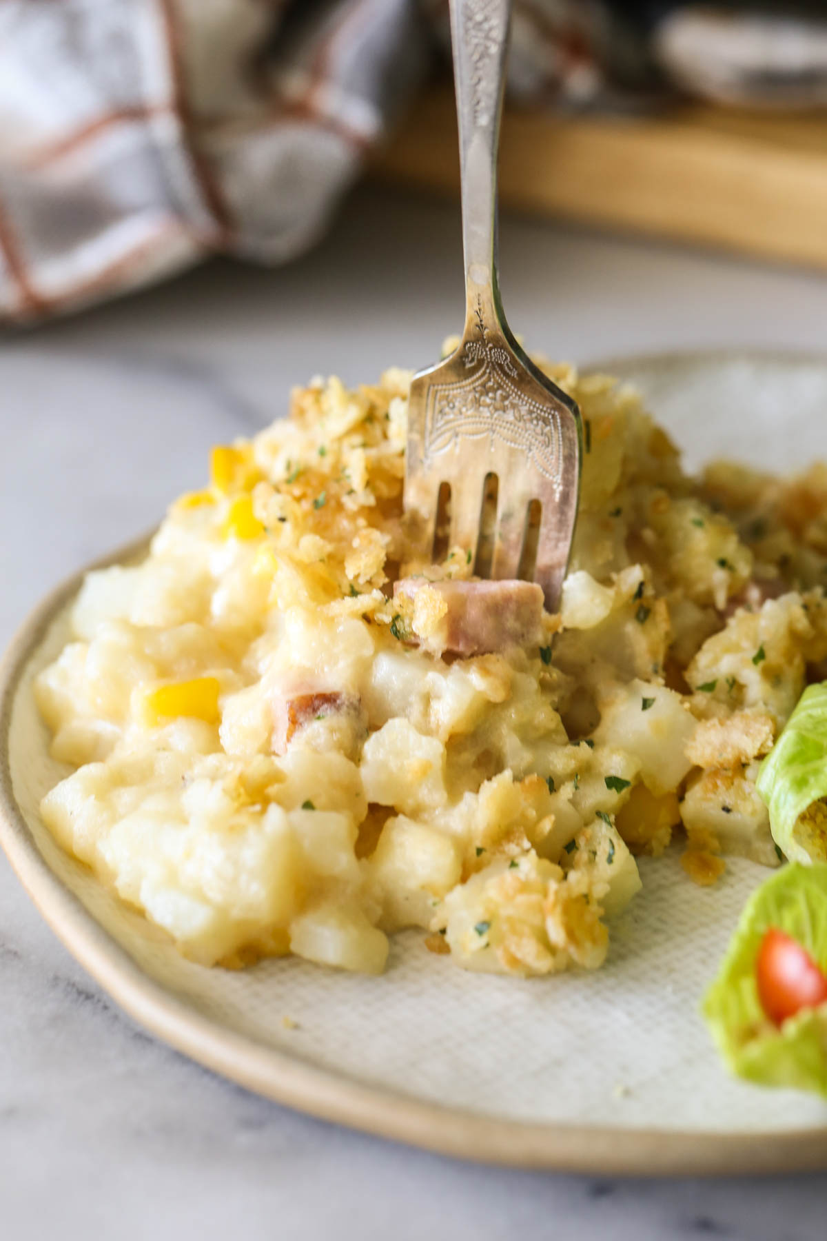 Close up shot of a serving of Cheesy Ham and Potato Skillet on a plate with a fork sticking in it.  