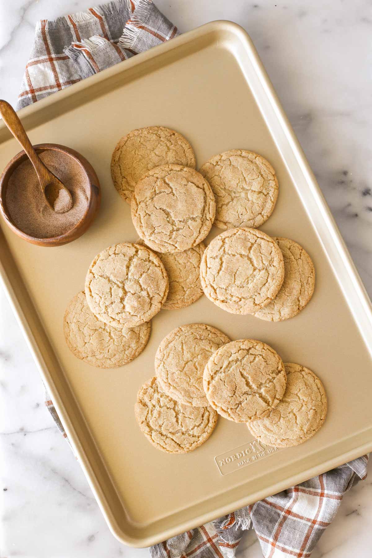 Overhead shot of Brown Butter Snickerdoodles on a baking sheet, along with a small wood bowl of cinnamon sugar with a small wooden spoon in it.